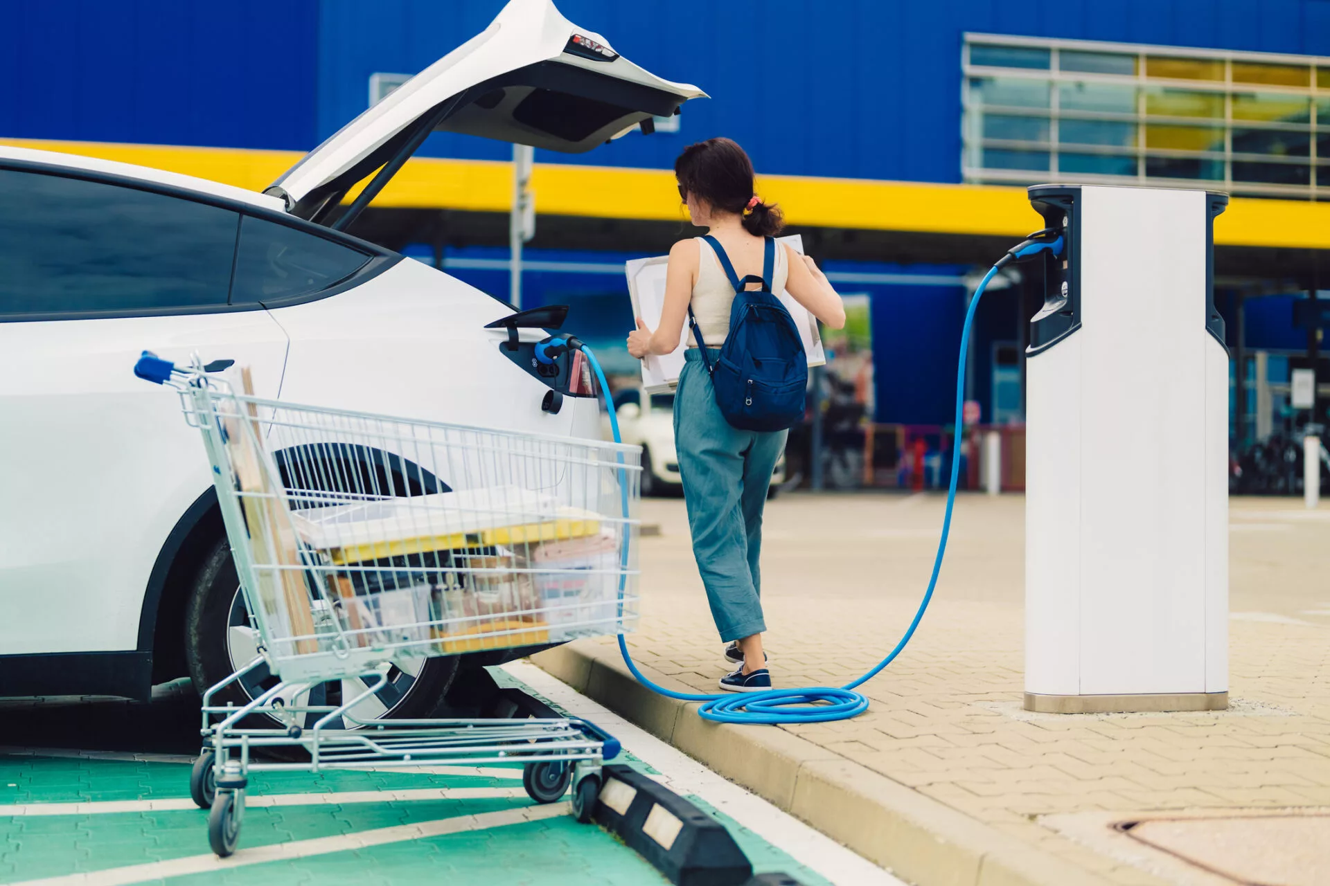 Woman charging car at electric vehicle charging station while shopping